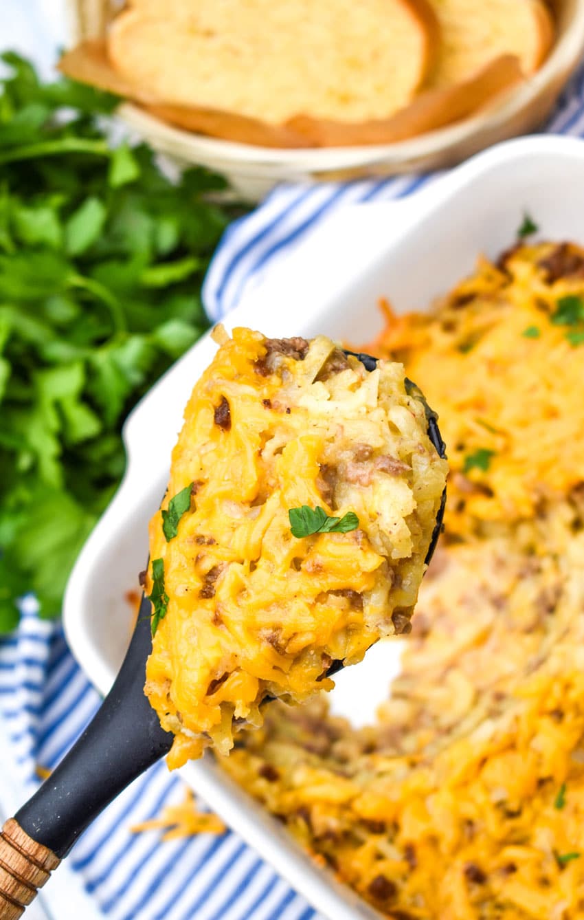 a black spoon holding up a scoop of cheesy hashbrown casserole with ground beef