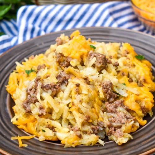 cheesy hashbrown casserole with ground beef on a brown plate with a fork resting on the side