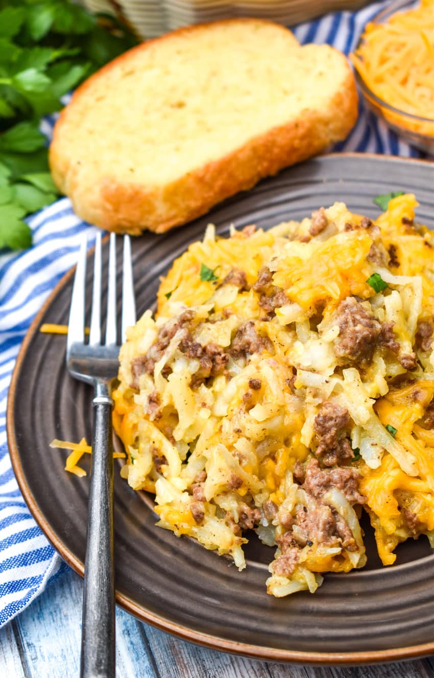 cheesy hashbrown casserole with ground beef on a brown plate with a fork resting on the side