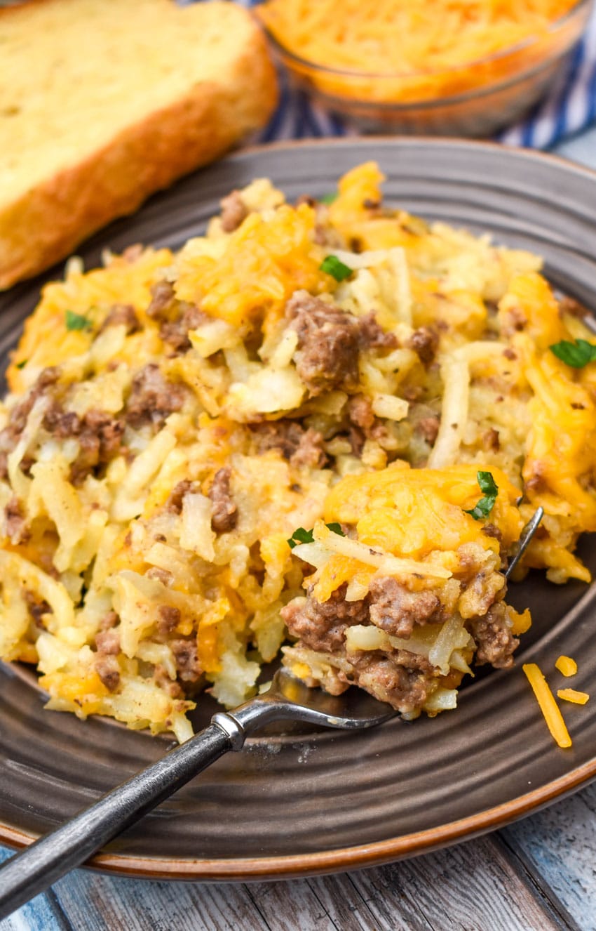 cheesy hashbrown casserole with ground beef on a brown plate with a fork resting on the side