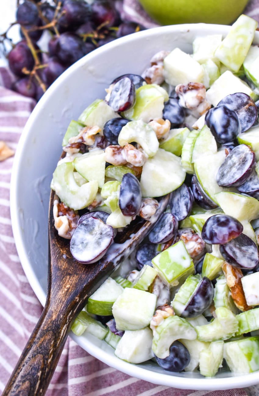 a wooden spoon scooping waldorf salad out of a white serving bowl