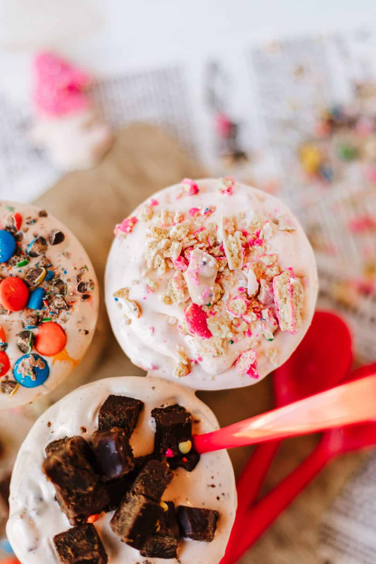 three different homemade blizzards on a wooden cutting board surrounded by candy pieces