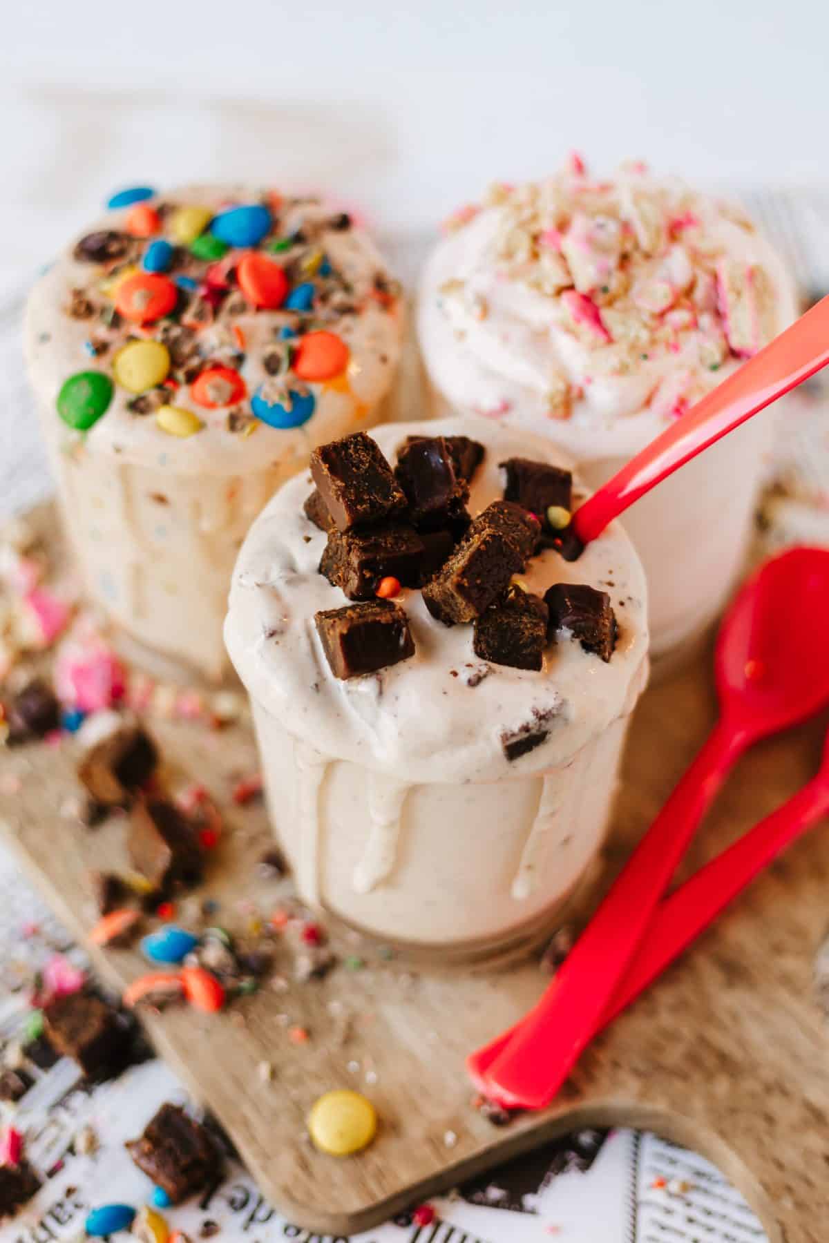 three different homemade blizzards on a wooden cutting board surrounded by candy pieces