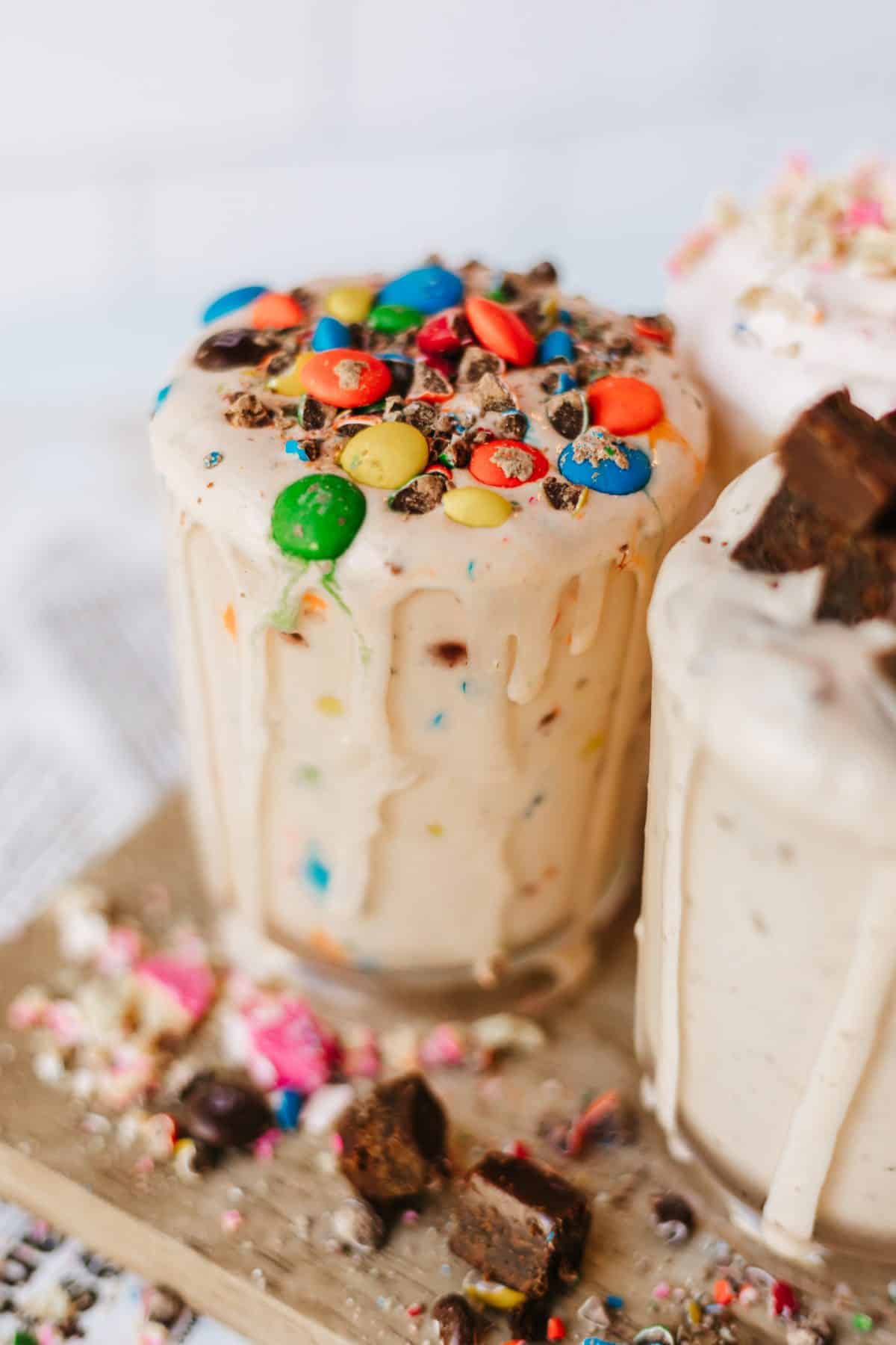 three different homemade blizzards on a wooden cutting board surrounded by candy pieces