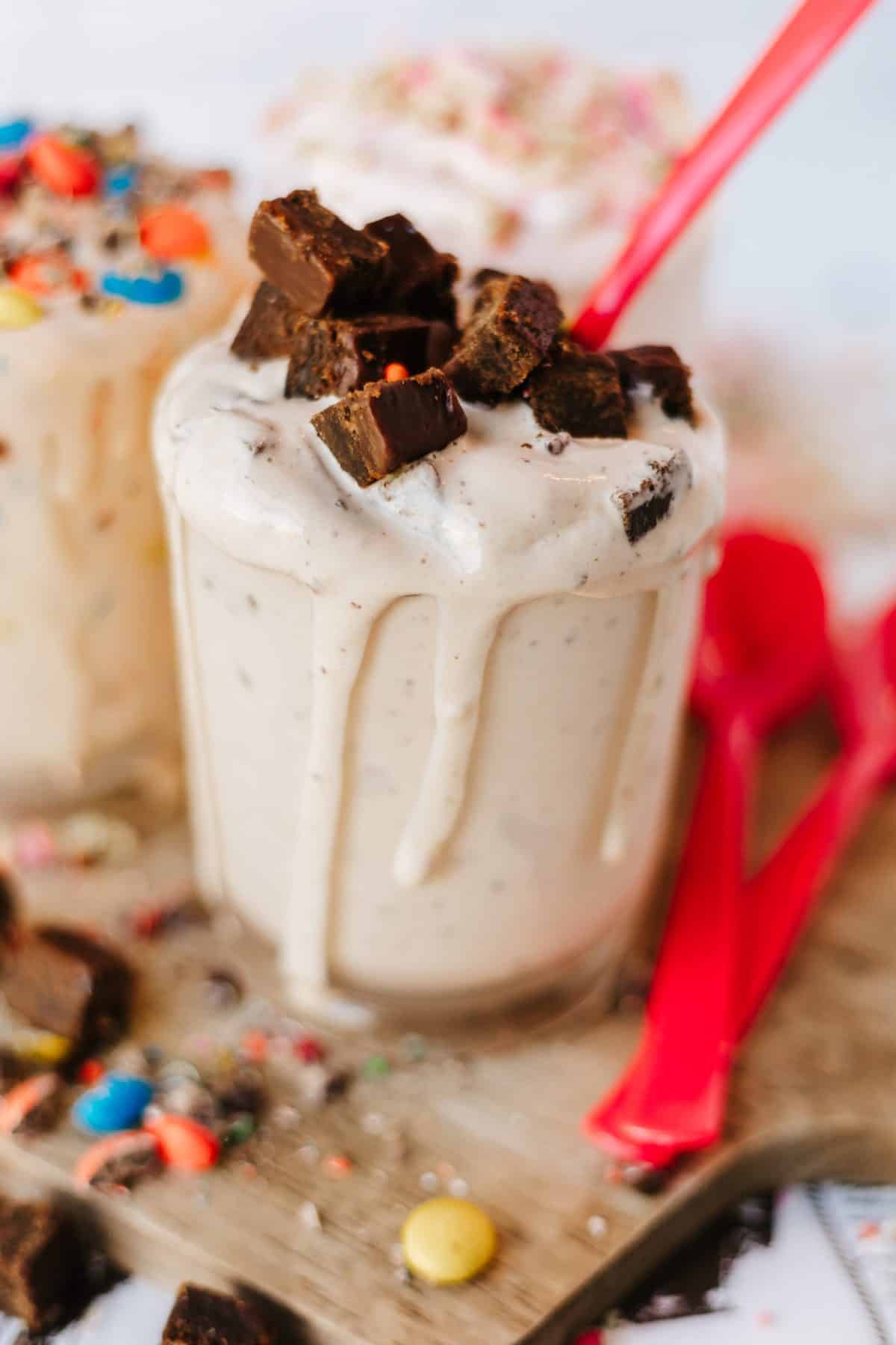 three different homemade blizzards on a wooden cutting board surrounded by candy pieces