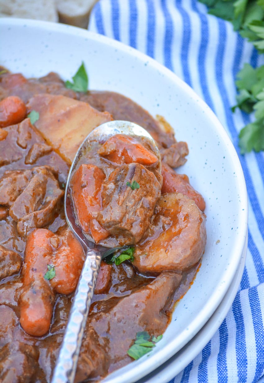 a silver spoon scooping french onion beef stew out of a shallow white bowl