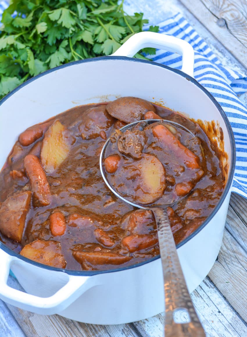 a silver ladle scooping french onion beef stew out of a white dutch oven