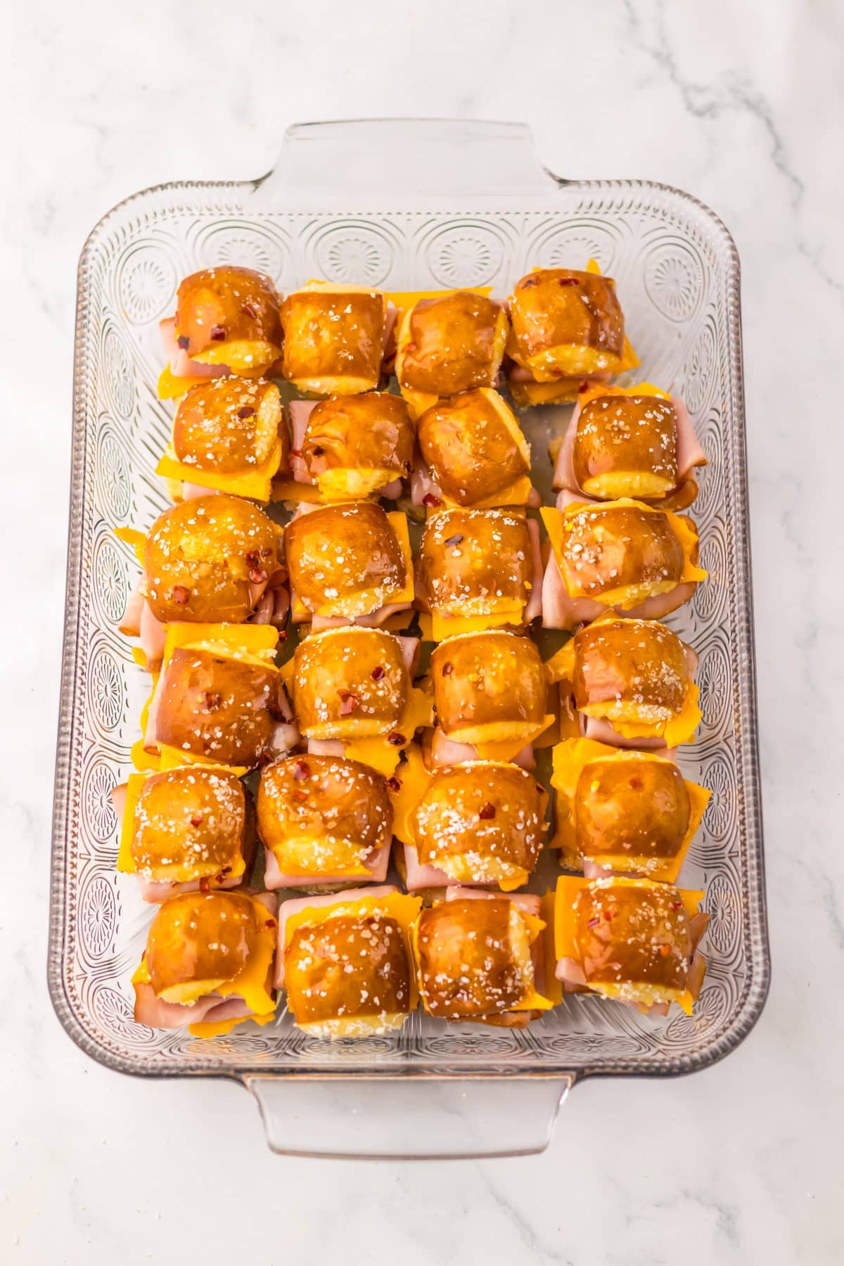 unbaked hot honey ham and cheese sliders arranged  in rows in a glass baking dish