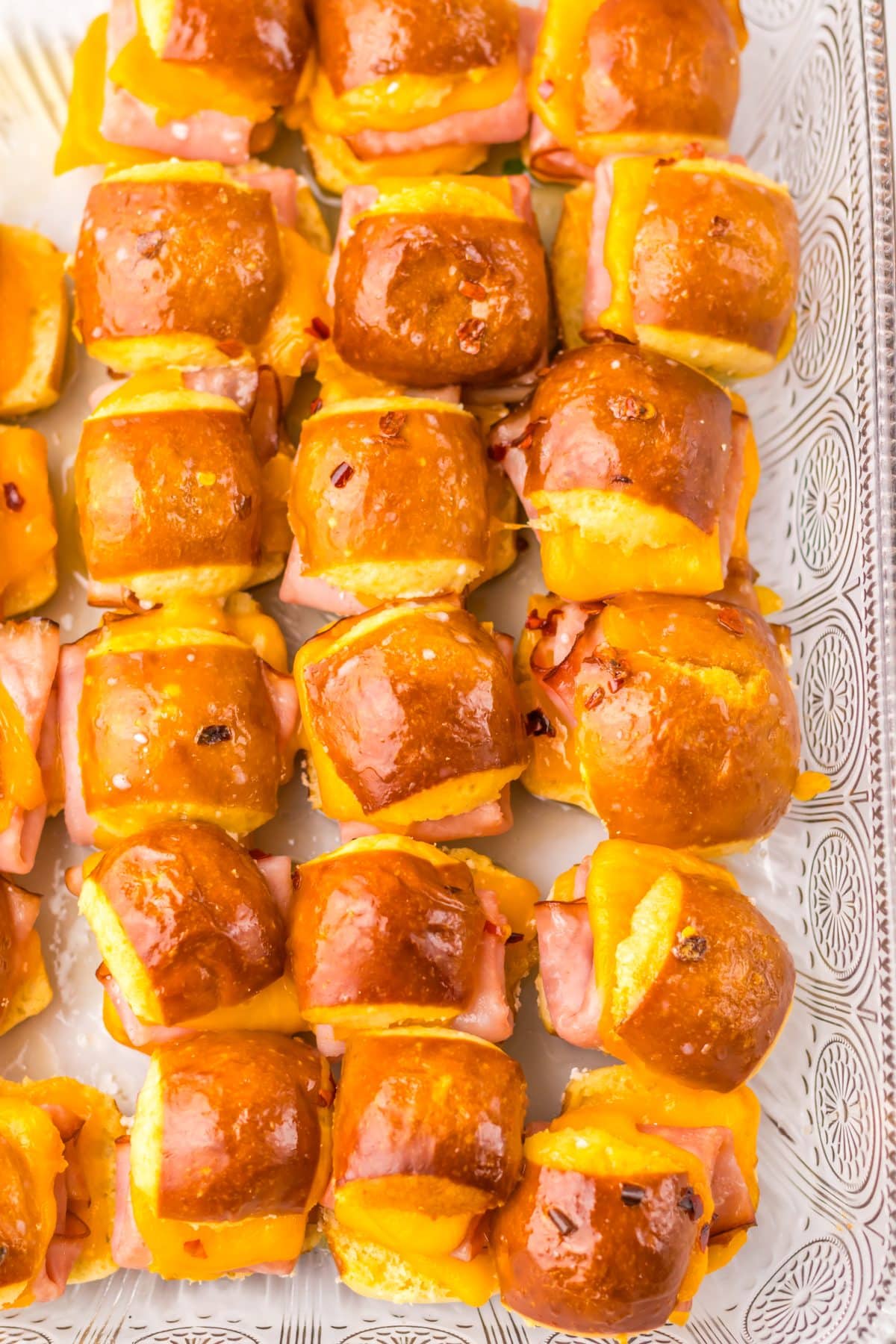 baked hot honey mini ham and cheese pretzel sliders arranged in rows in a glass baking dish