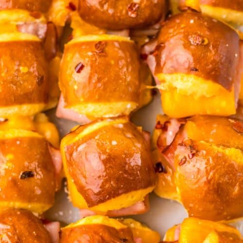 baked hot honey mini ham and cheese pretzel sliders arranged in rows in a glass baking dish