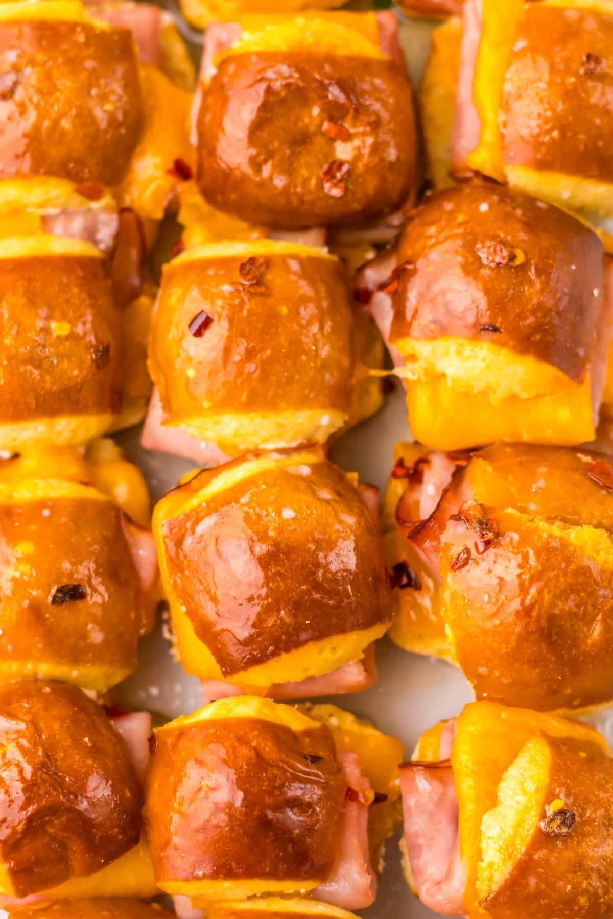 baked hot honey mini ham and cheese pretzel sliders arranged in rows in a glass baking dish