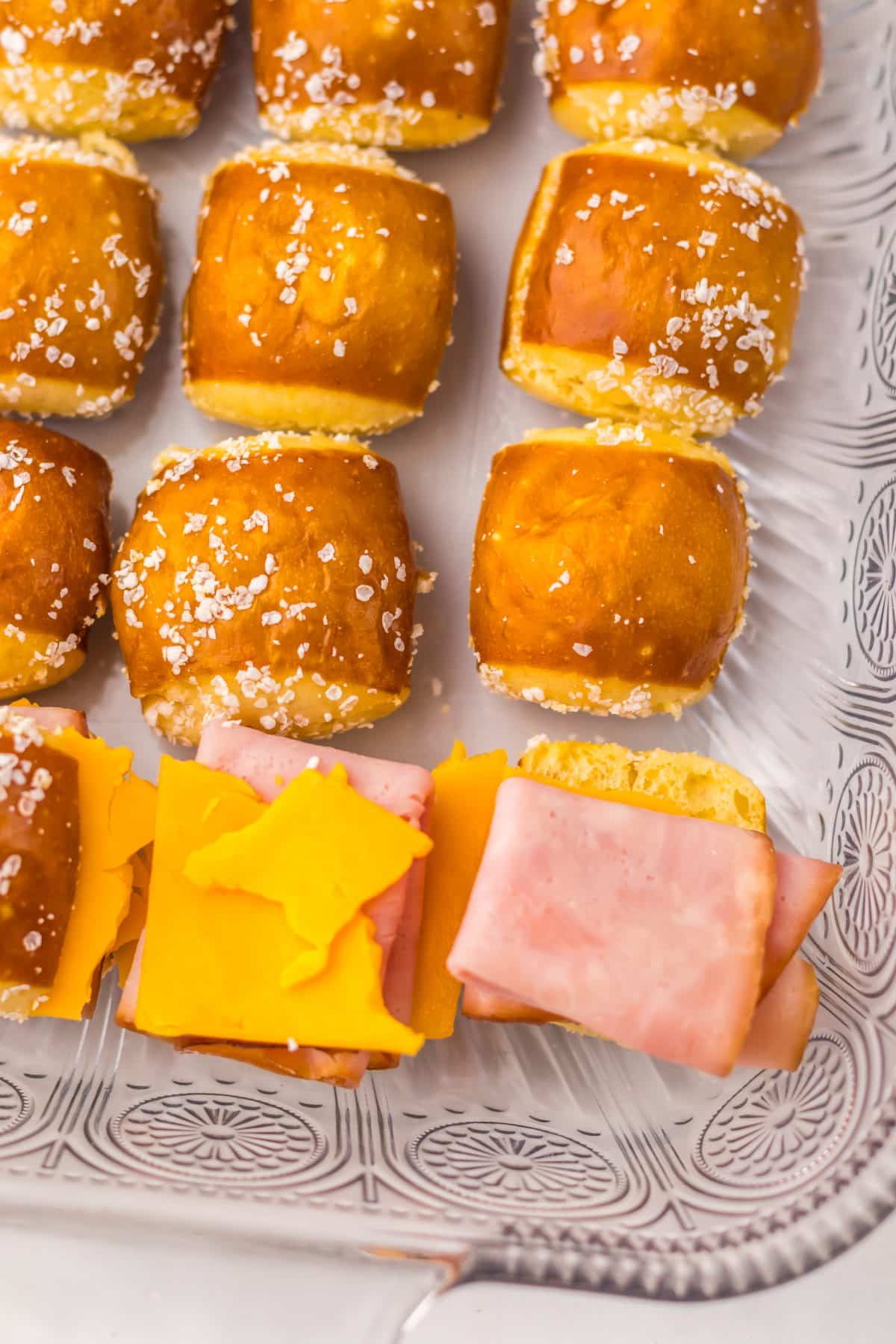 hot honey ham and pretzel sliders being assembled in a glass baking dish