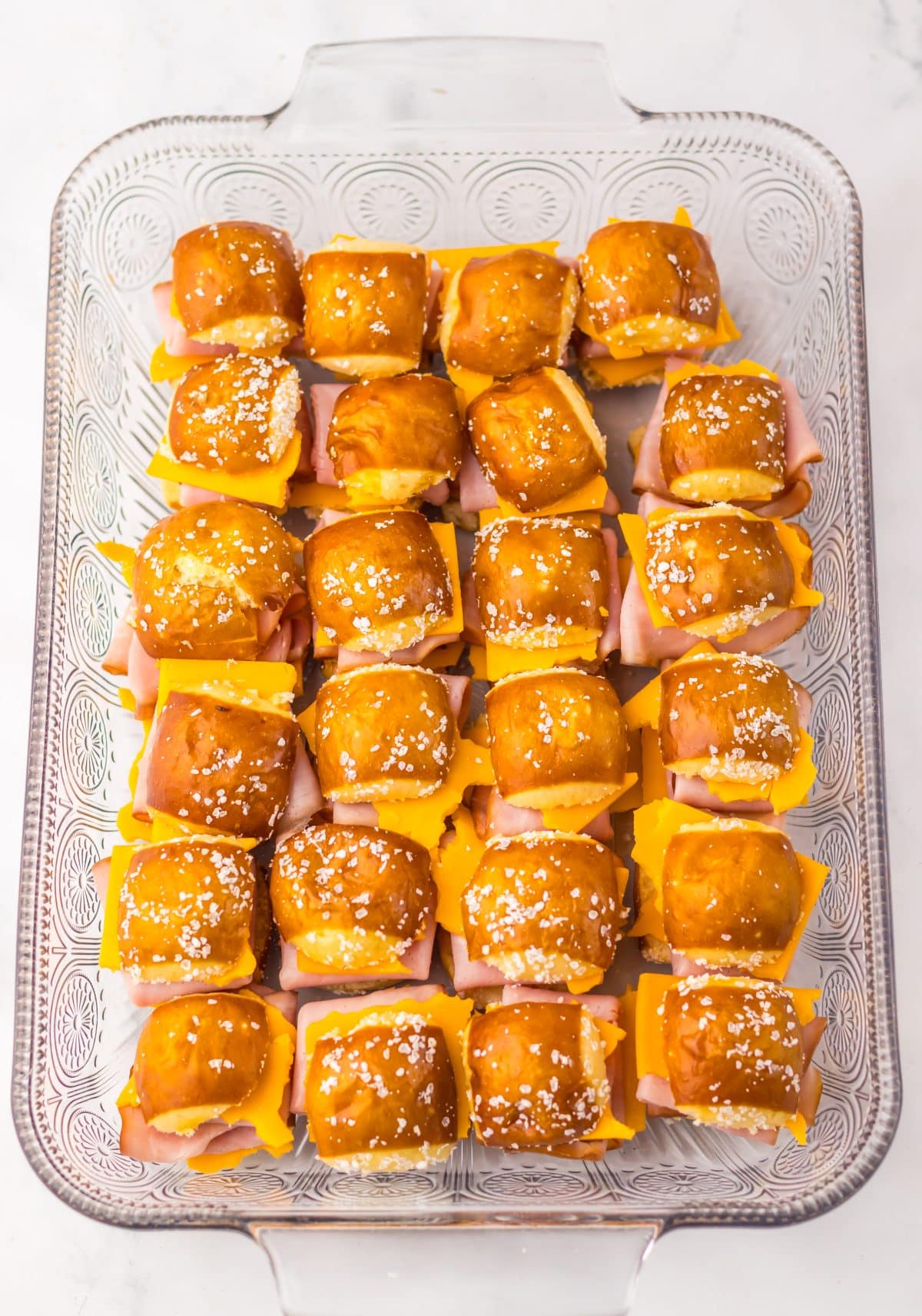 unbaked hot honey ham and cheese sliders arranged  in rows in a glass baking dish