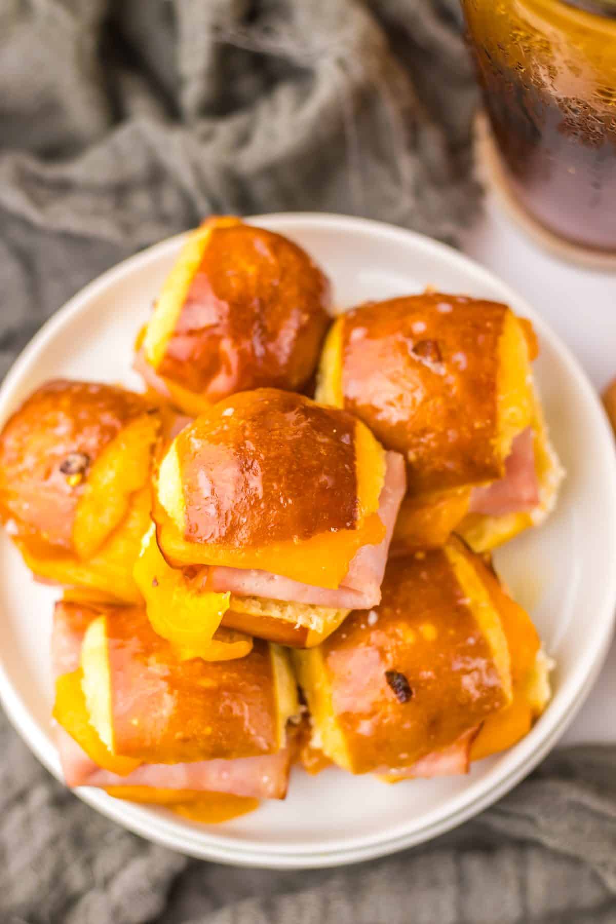 hot honey ham and cheese pretzel sliders piled high on a small white appetizer plus