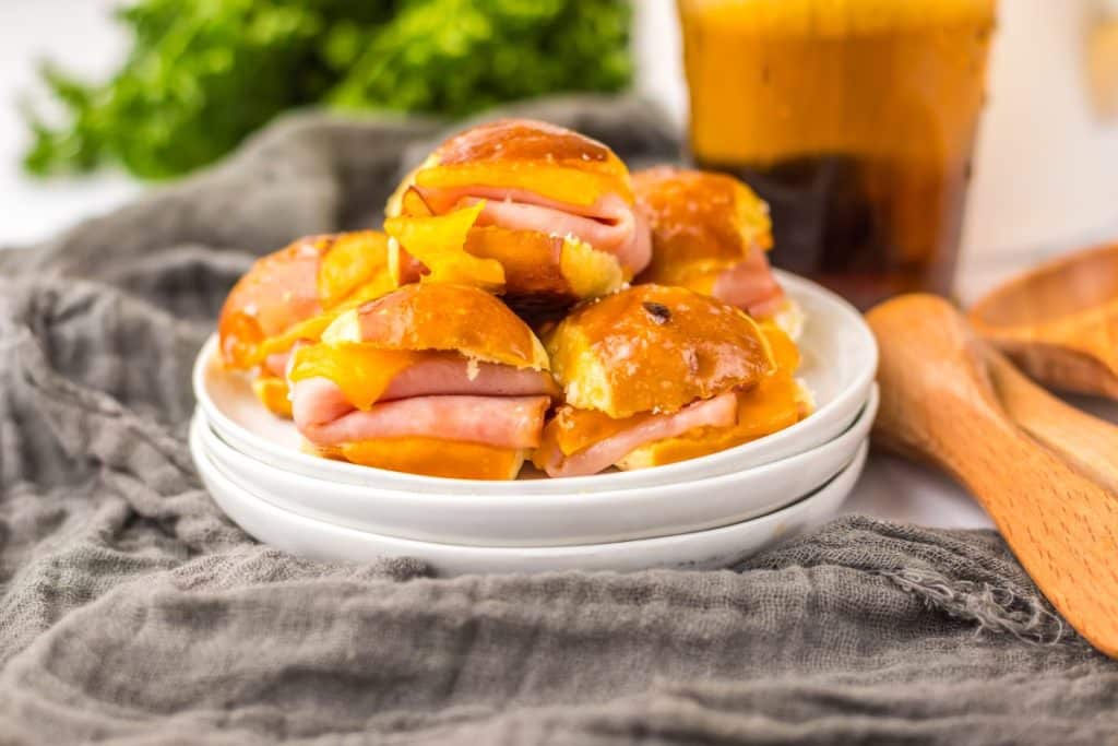 hot honey ham and cheese pretzel sliders piled high on a small white appetizer plus