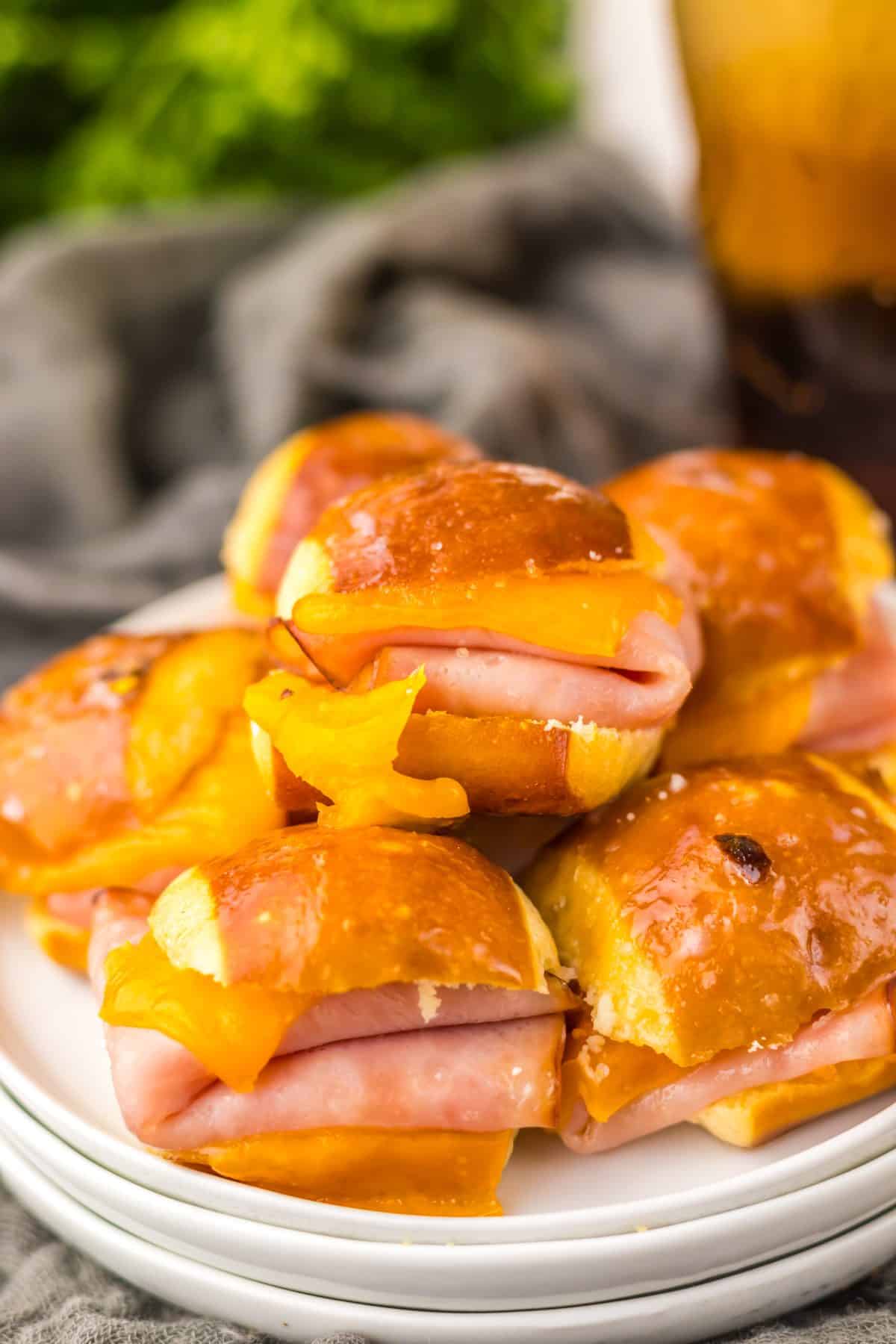 hot honey ham and cheese pretzel sliders piled high on a small white appetizer plus