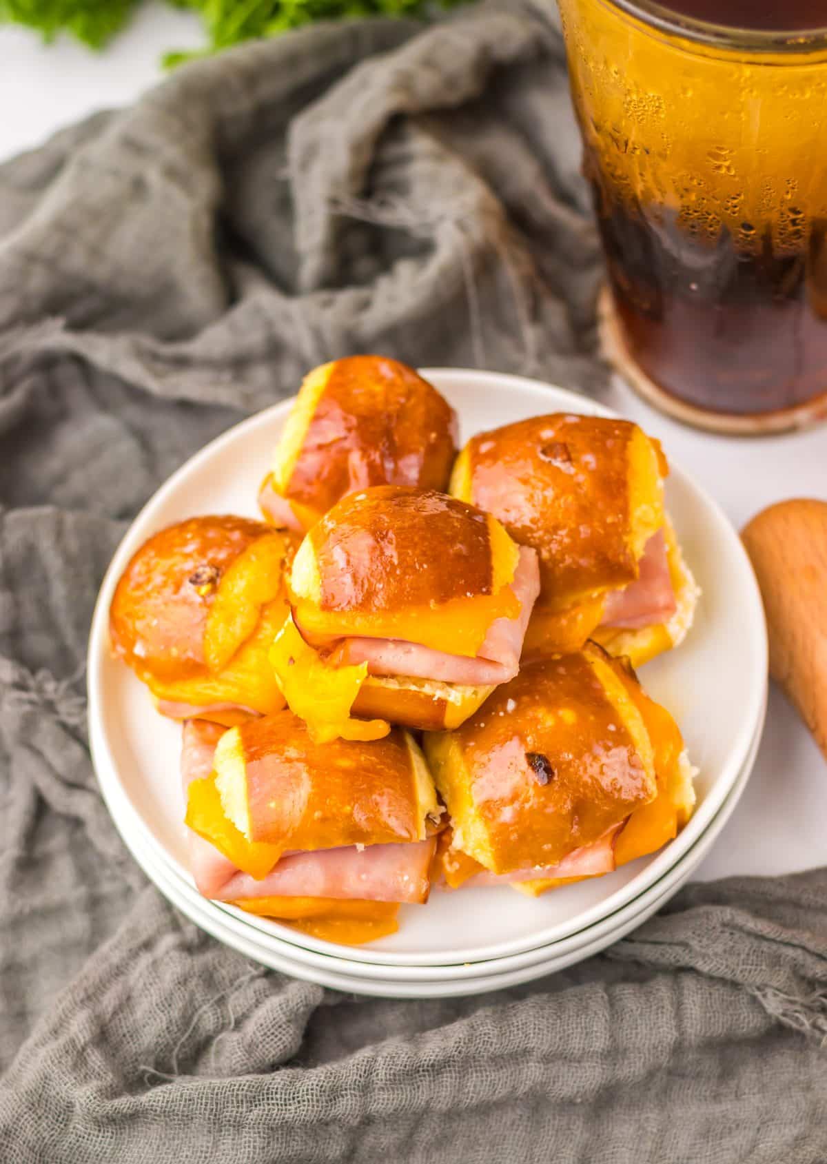 hot honey ham and cheese pretzel sliders piled high on a small white appetizer plus