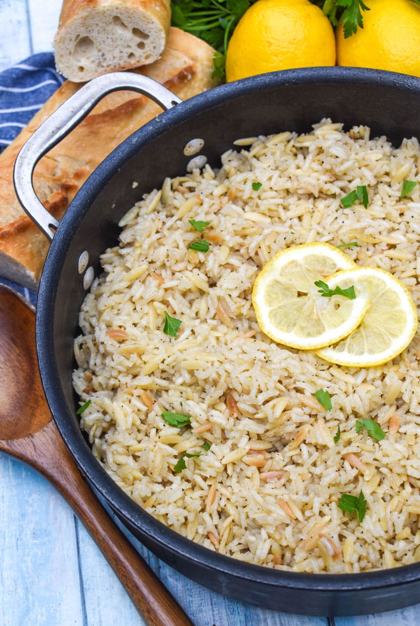lemon rice topped with fresh green herbs and lemon slices in a large black skillet