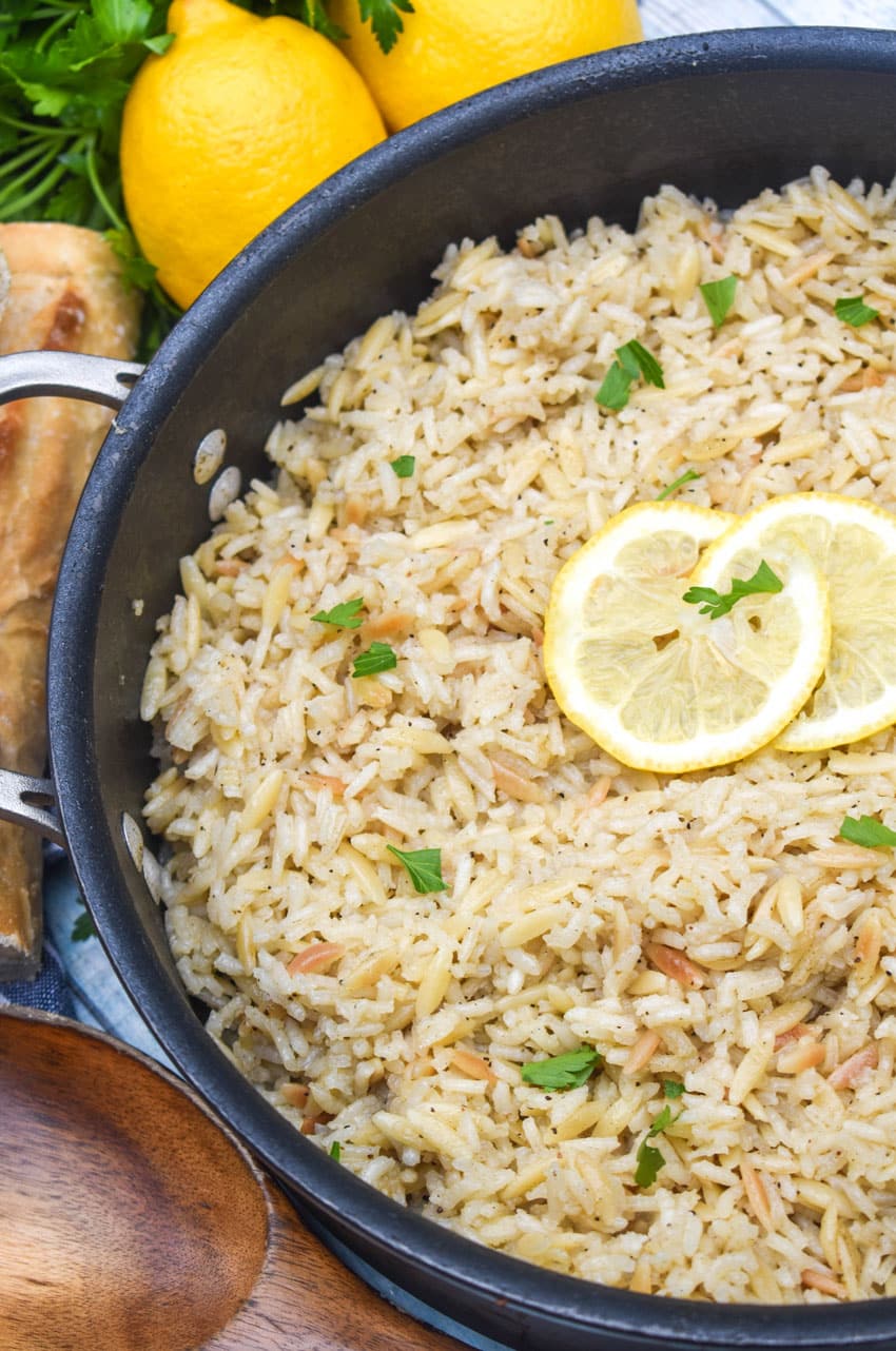 lemon rice topped with fresh green herbs and lemon slices in a large black skillet