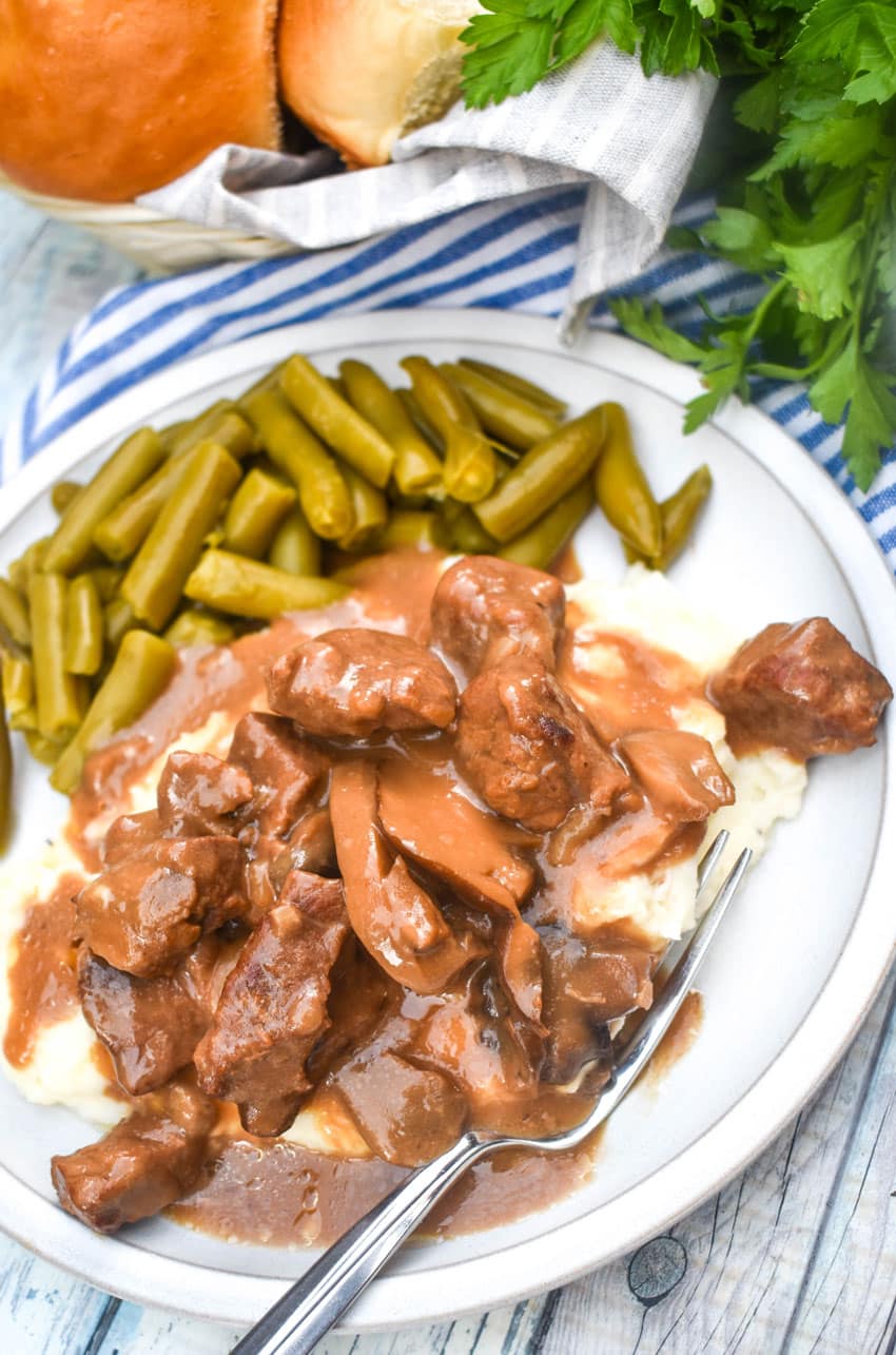 no peek beef tips over mashed potatoes next to green beans on a white dinner plate