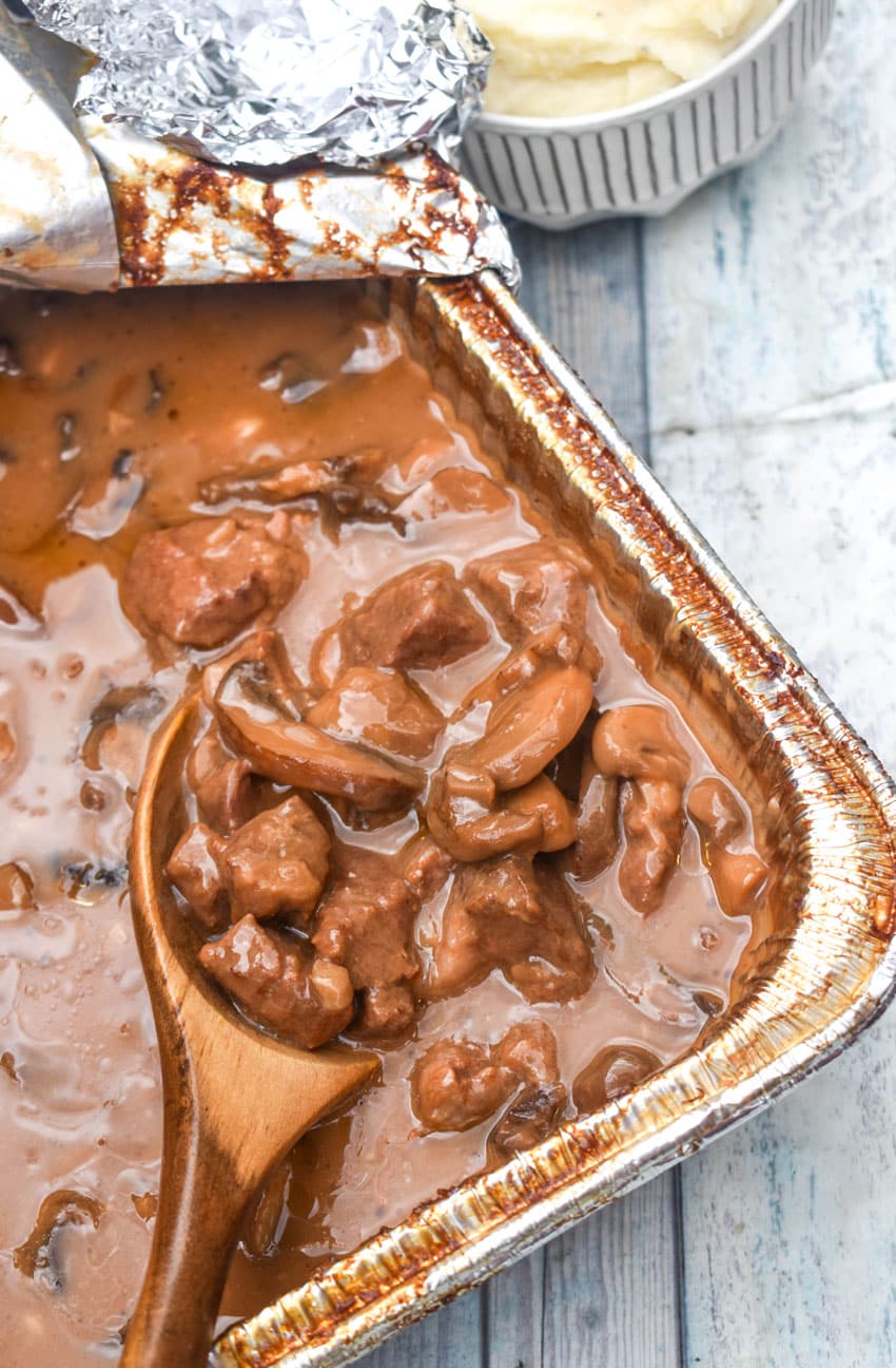 a wooden spoon scooping no peek beef tips out of an aluminum tray