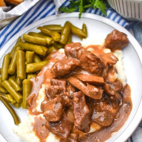 no peek beef tips over mashed potatoes next to green beans on a white dinner plate