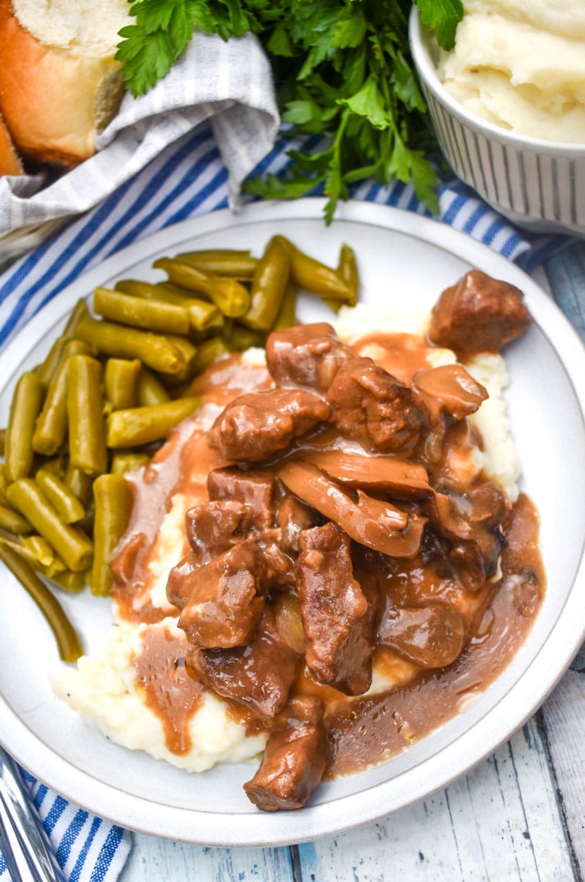 no peek beef tips over mashed potatoes next to green beans on a white dinner plate