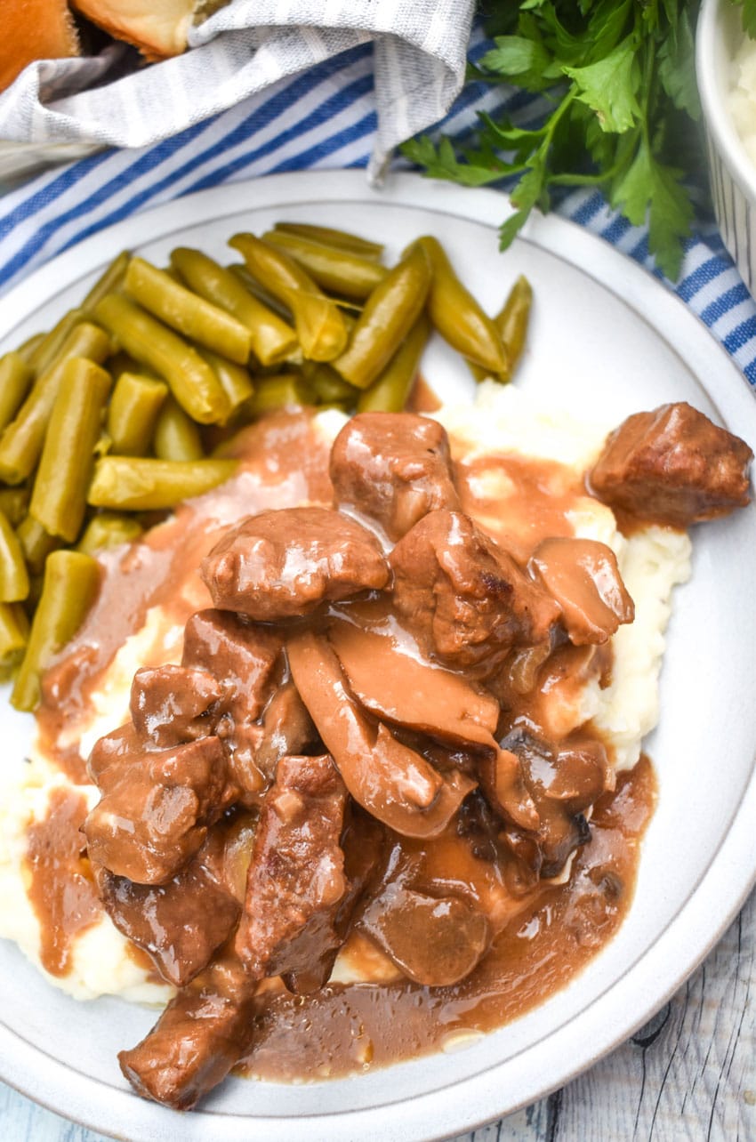 no peek beef tips over mashed potatoes next to green beans on a white dinner plate