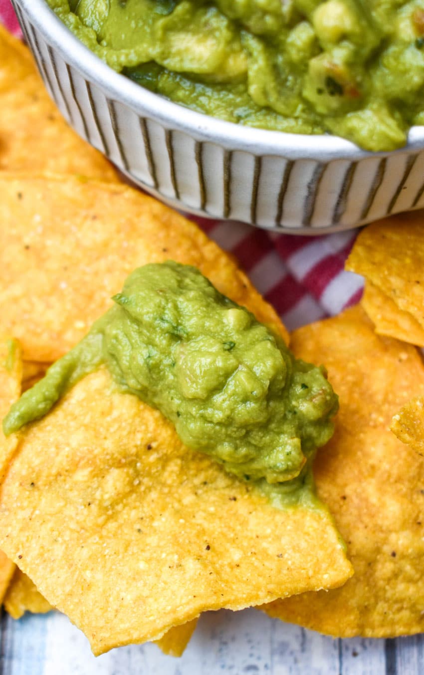 a tortilla chip topped with homemade guacamole resting on a bed of homemade chips
