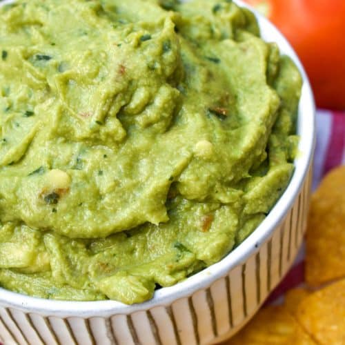 the best homemade guacamole in a white bowl surrounded by tortilla chips