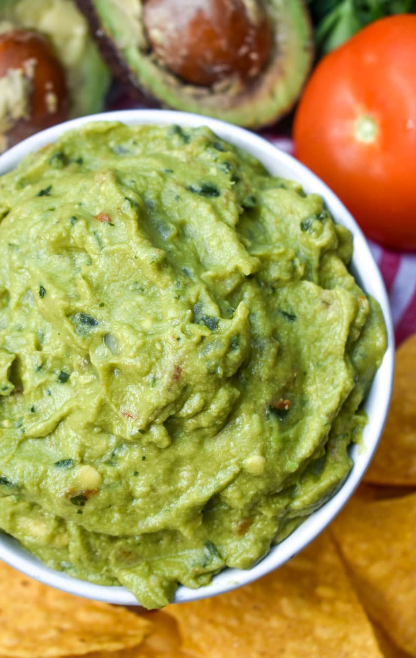 the best homemade guacamole in a white bowl surrounded by tortilla chips