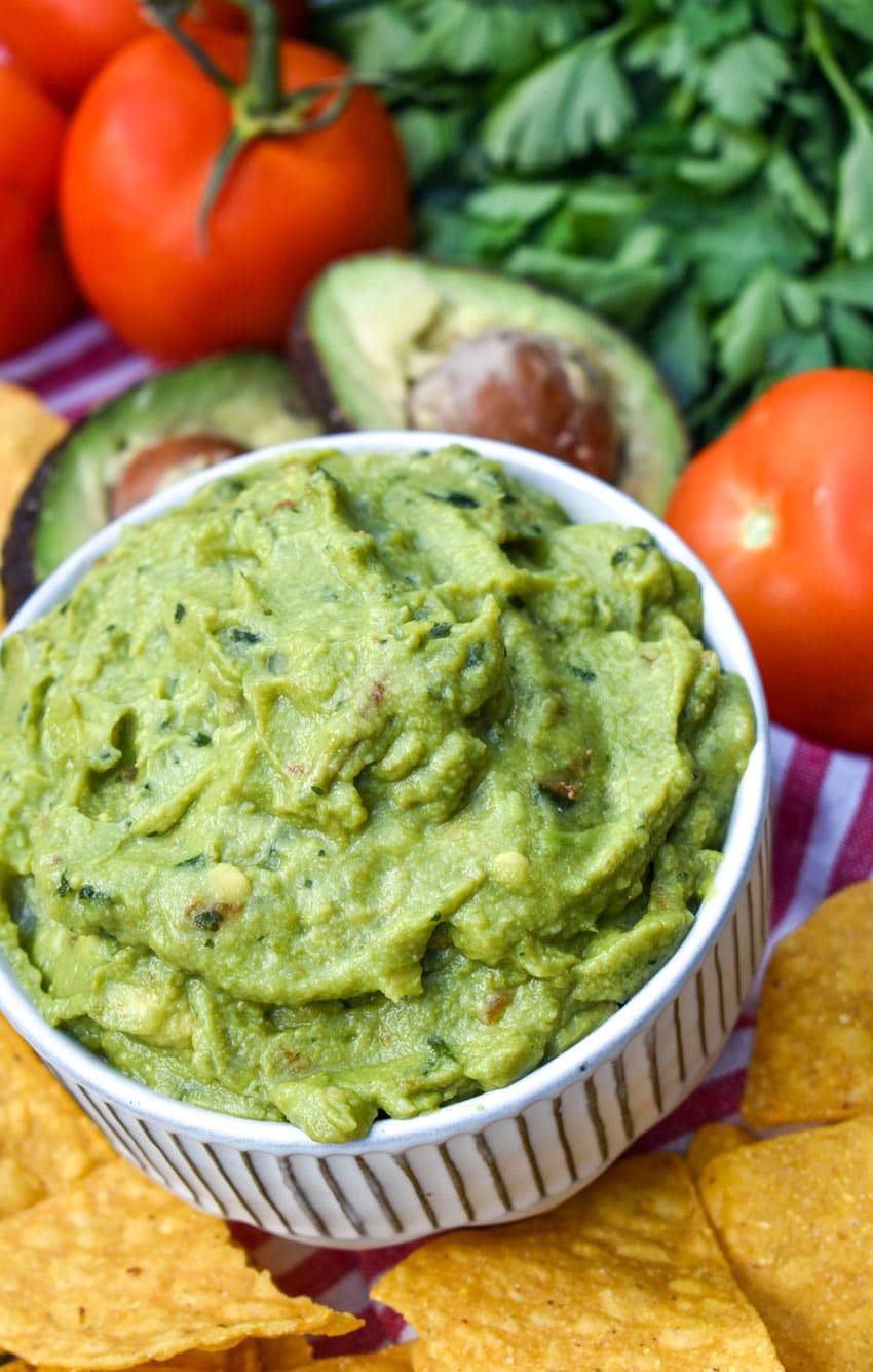 the best homemade guacamole in a white bowl surrounded by tortilla chips