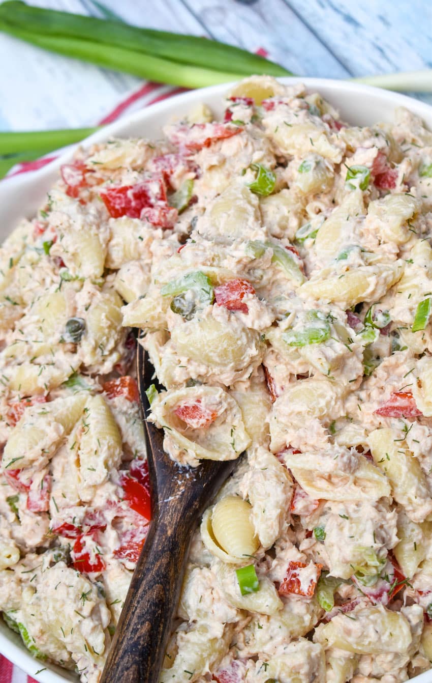 A wooden spoon scooping canned salmon pasta salad out of a white serving dish