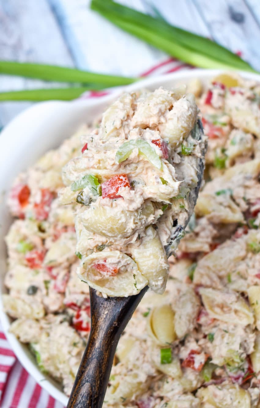 a wooden spoon holding up a scoop of canned salmon pasta salad
