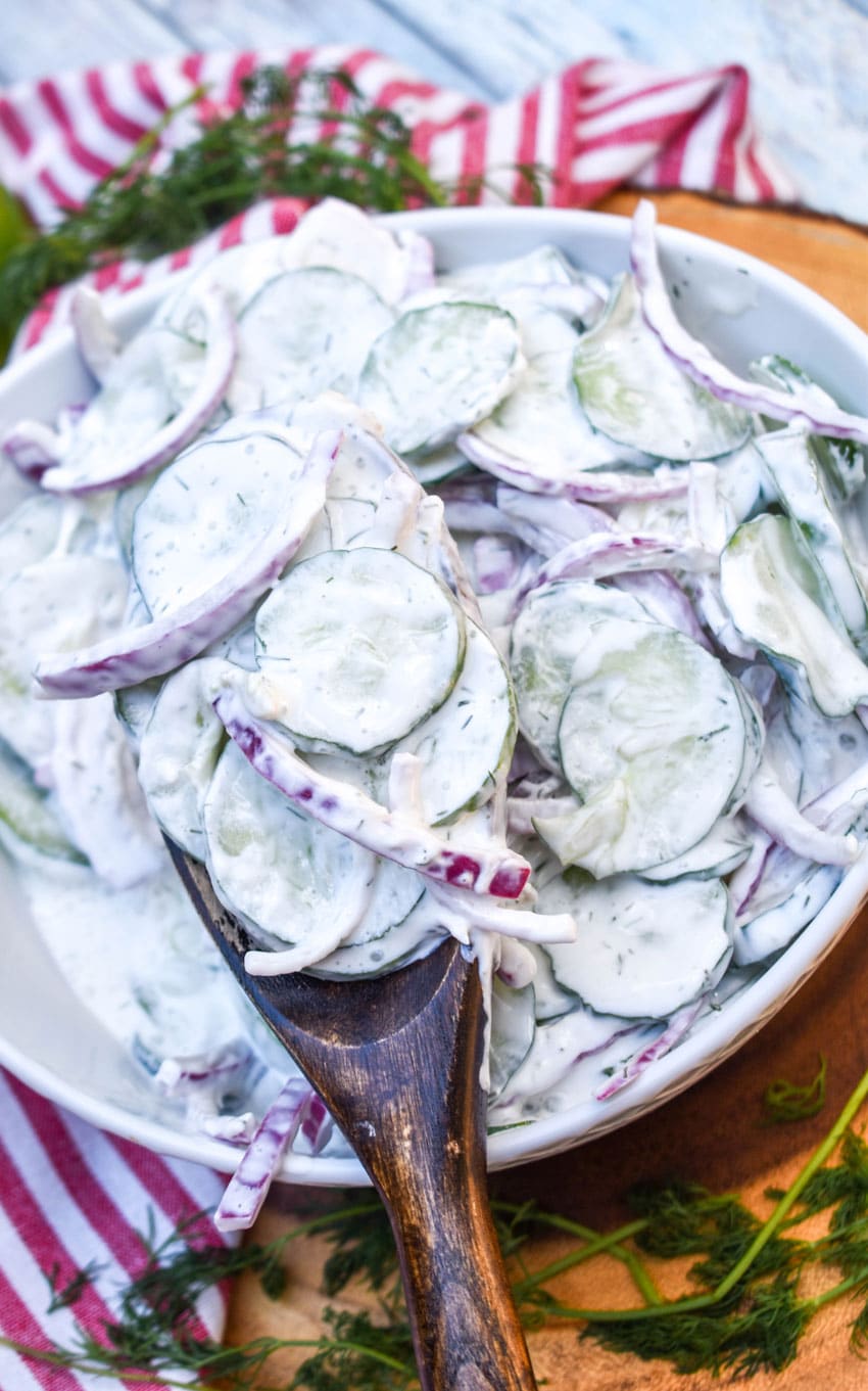 a wooden spoon scooping creamy cucumber salad out of a white serving bowl