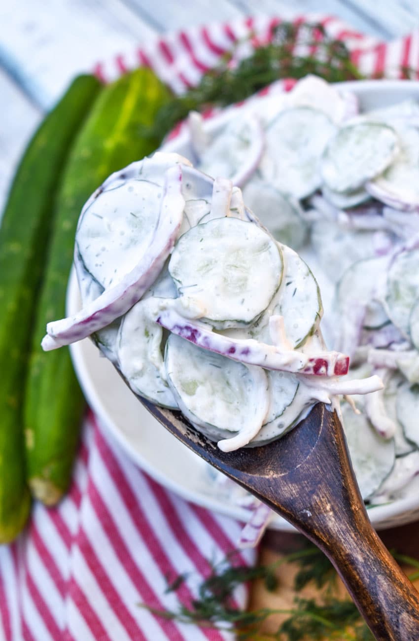 a wooden spoon holding up a scoop of creamy cucumber salad