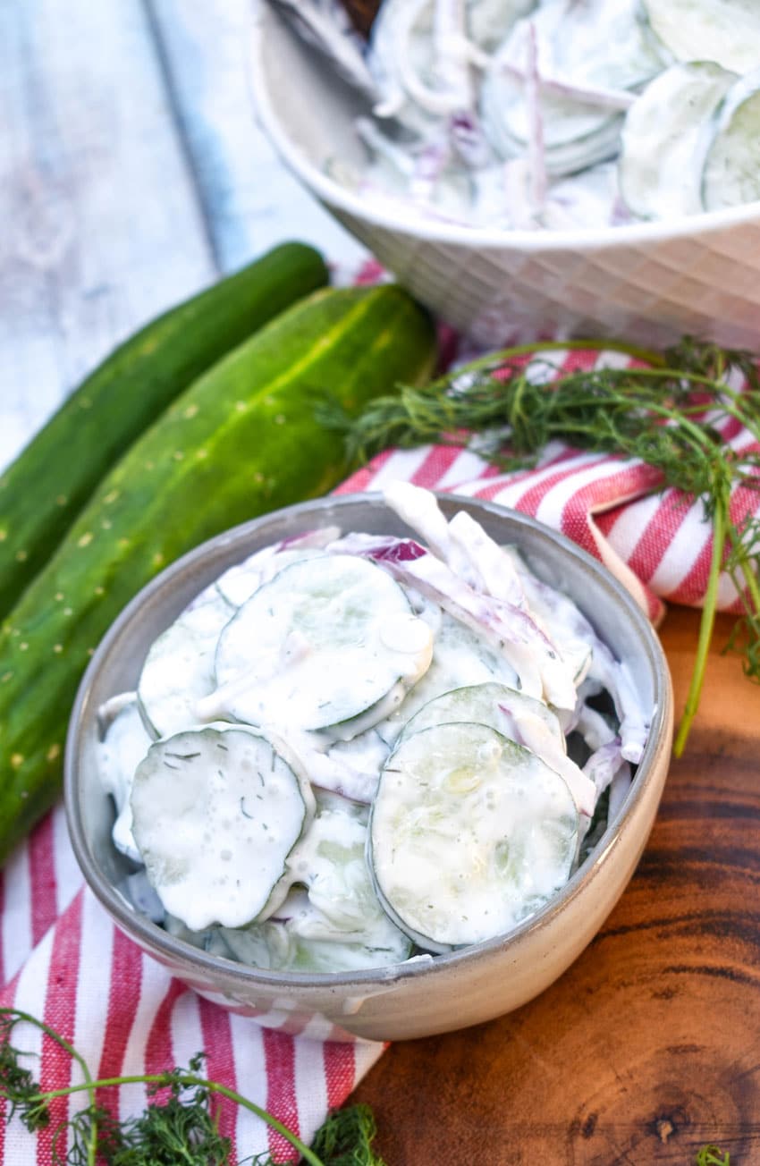 creamy cucumber salad in a small gray bowl on a wooden cutting board