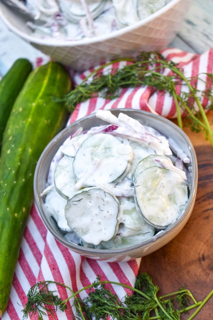 creamy cucumber salad in a small gray bowl on a wooden cutting board