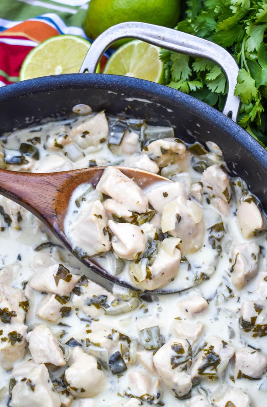 A WOODEN SPOON SCOOPING CREAMY POBLANO CHICKEN OUT OF A BLACK SKILLET