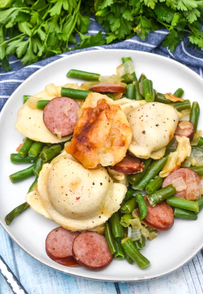 kielbasa, pierogi, and vegetables on a small white plate