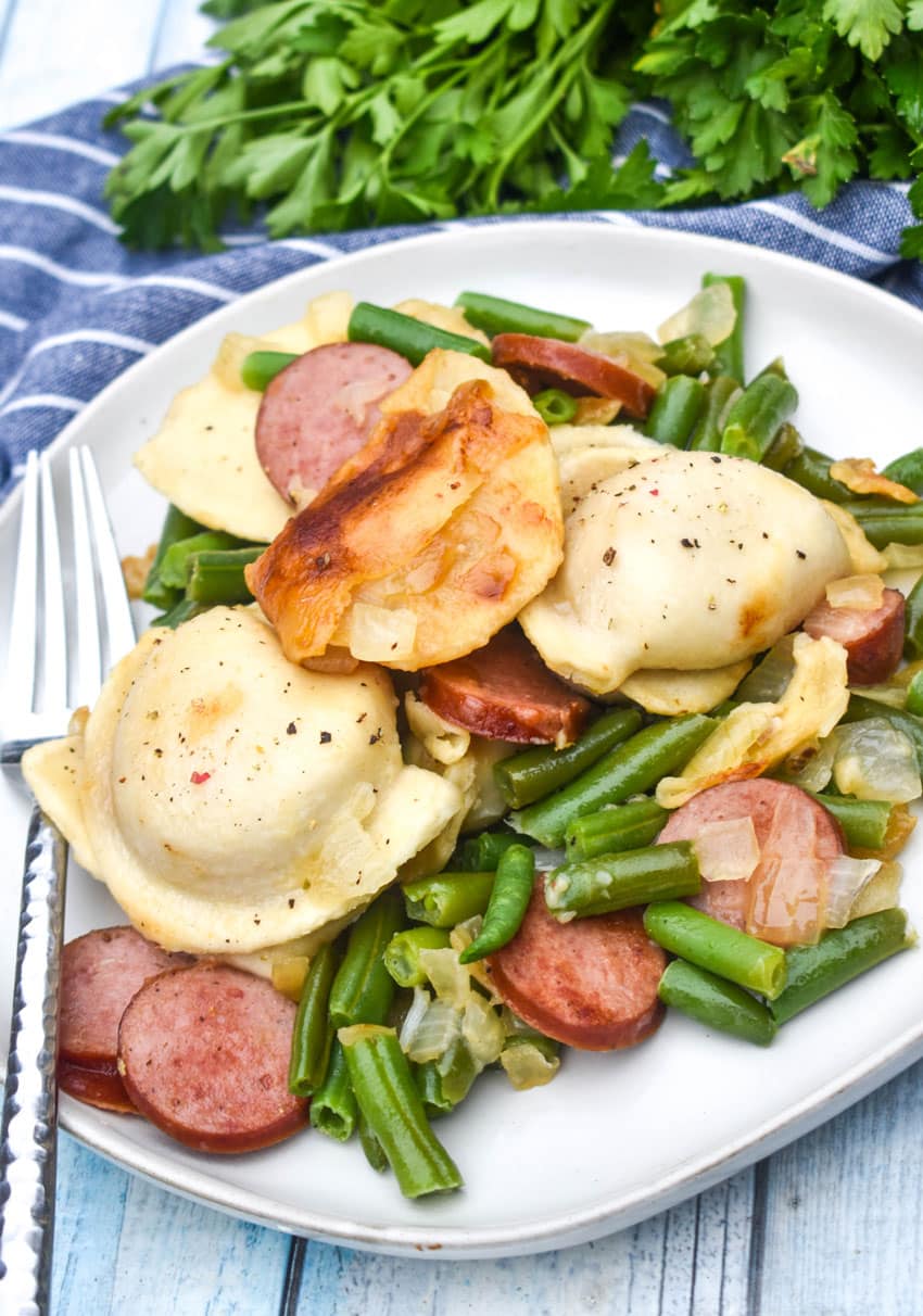 kielbasa, pierogi, and vegetables on a small white plate with a silver fork resting on the side