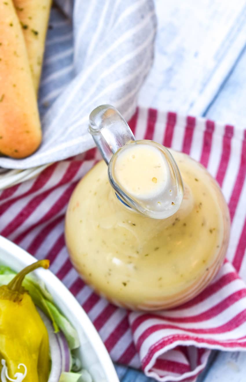 copycat olive garden salad dressing in a glass cruet in front of a salad bowl