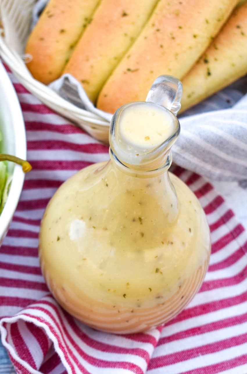 copycat olive garden salad dressing in a glass cruet in front of a salad bowl