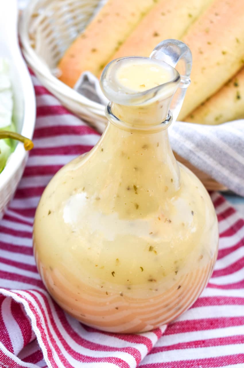 copycat olive garden salad dressing in a glass cruet in front of a salad bowl