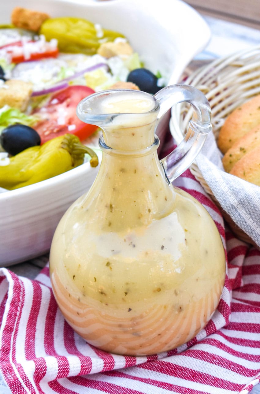 copycat olive garden salad dressing in a glass cruet in front of a salad bowl