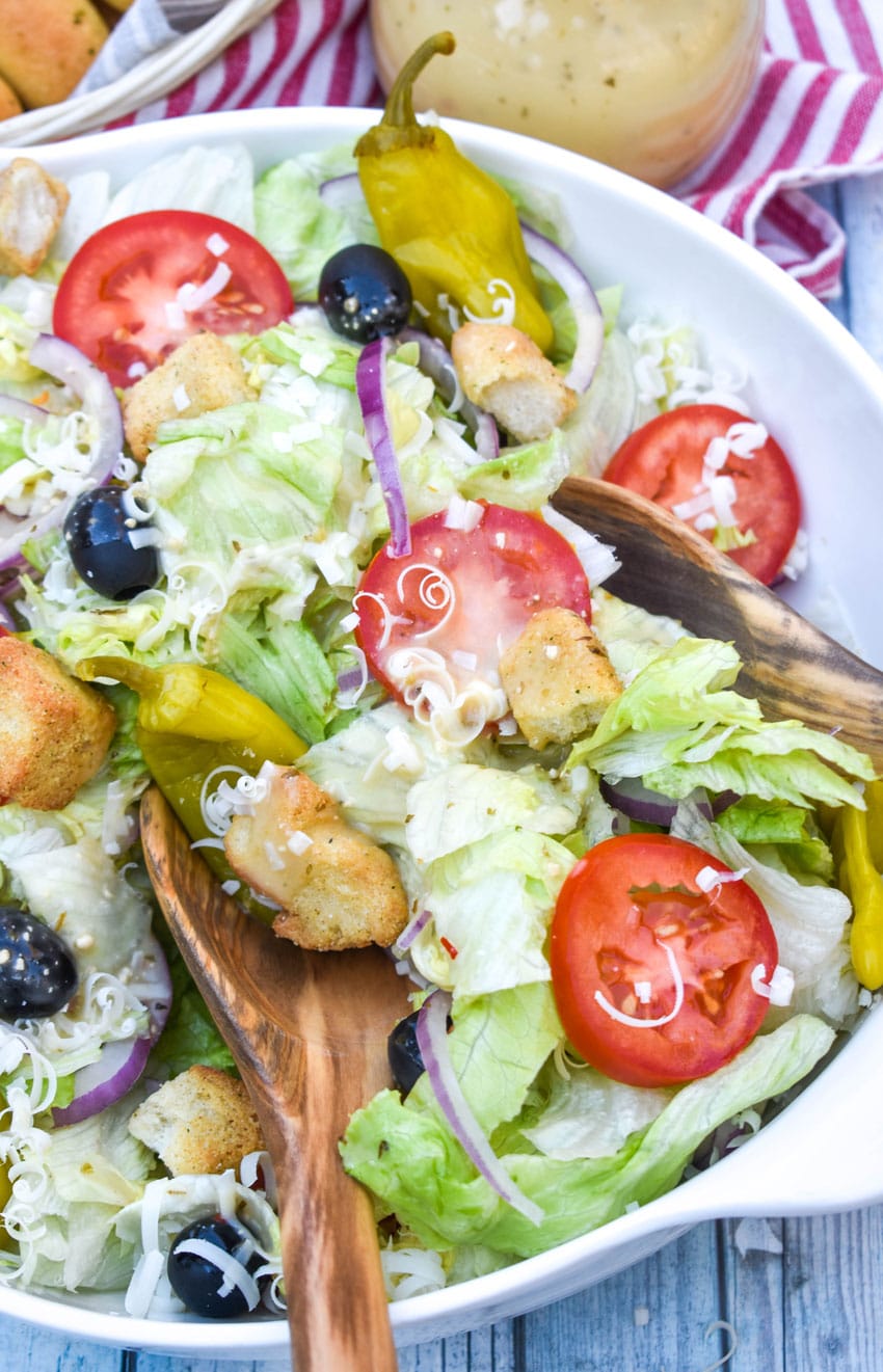 wooden salad utensils tossing a homemade olive garden salad copycat in a white salad bowl