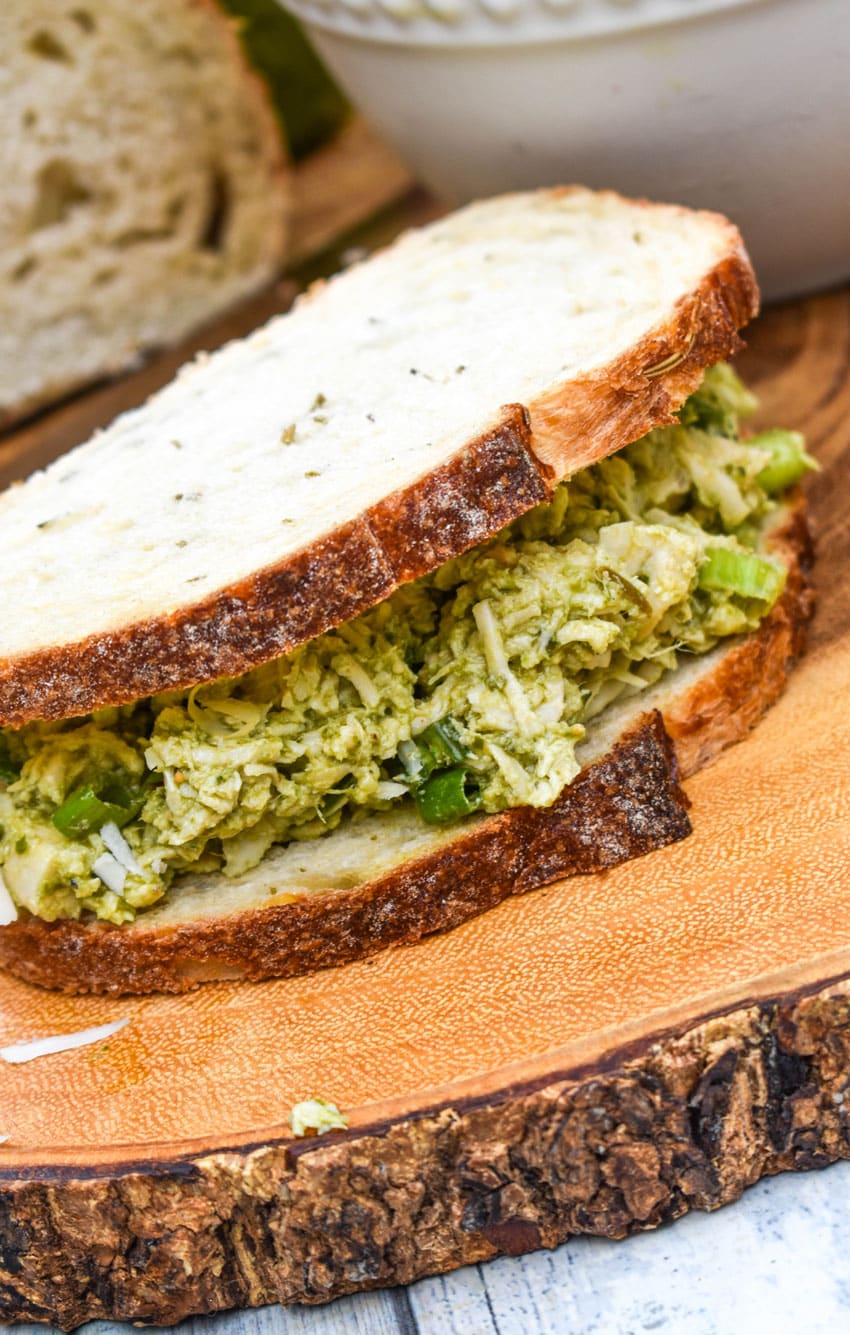 a pesto chicken salad sandwich on sourdough bread resting on a wooden cutting board