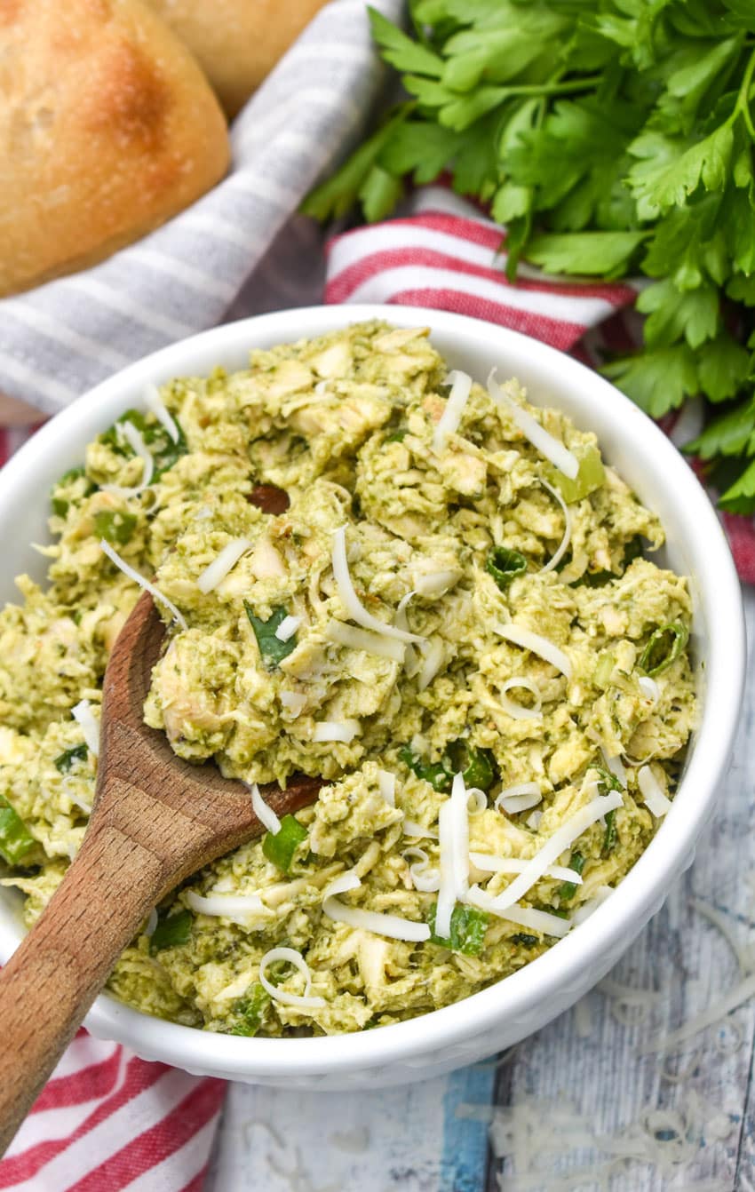 a wooden spoon scooping pesto chicken salad out of a white bowl