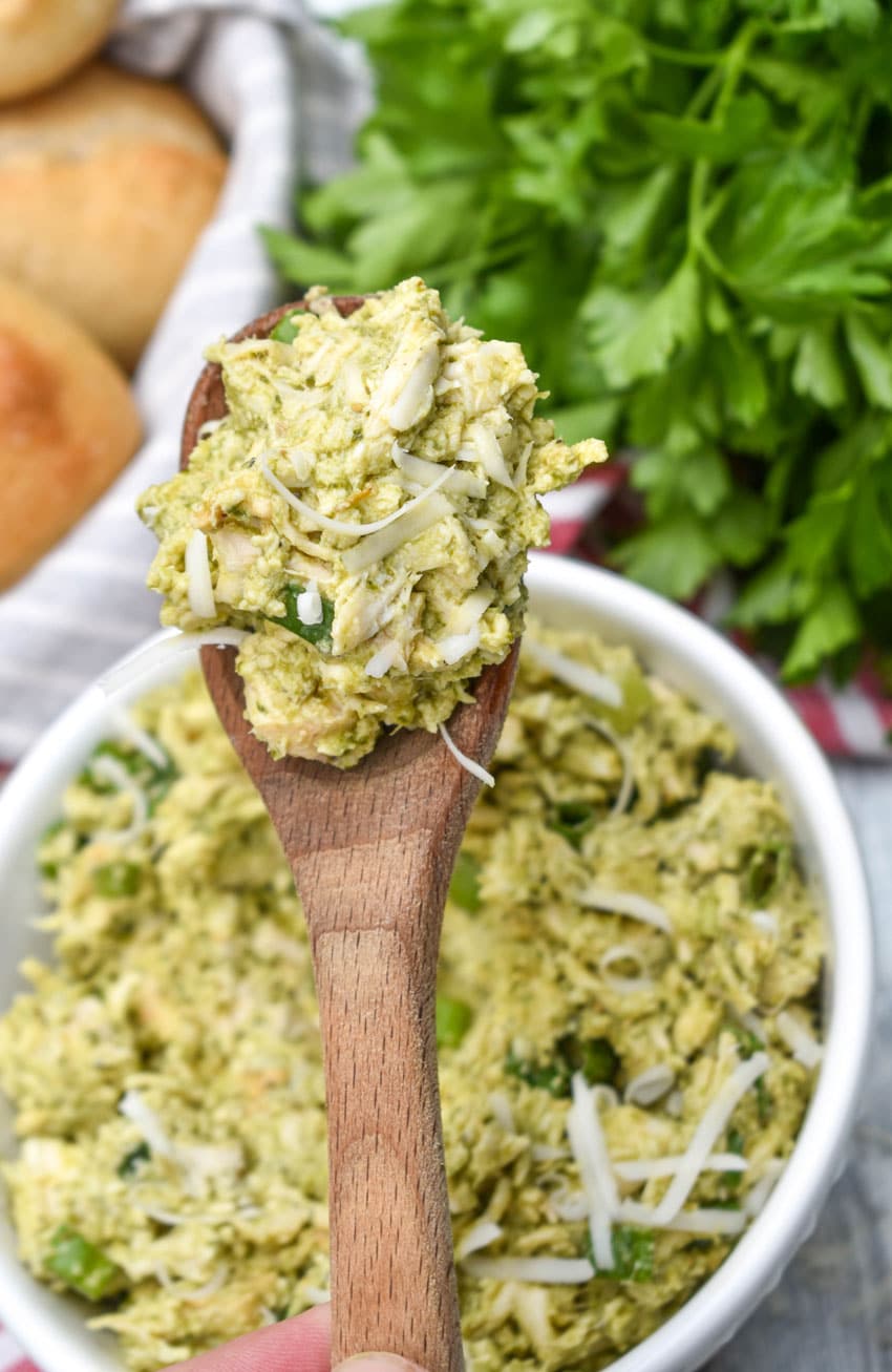 a wooden spoon holding up a scoop of pesto chicken salad