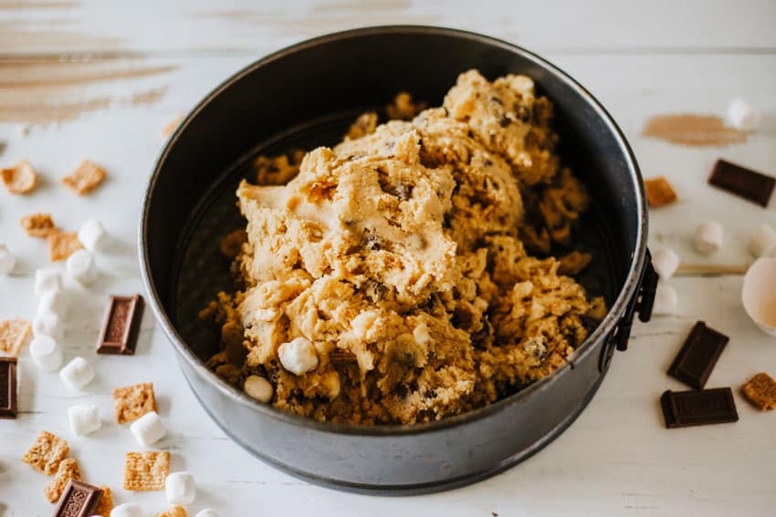 cookie cake batter being spread in a dark metal springform pan